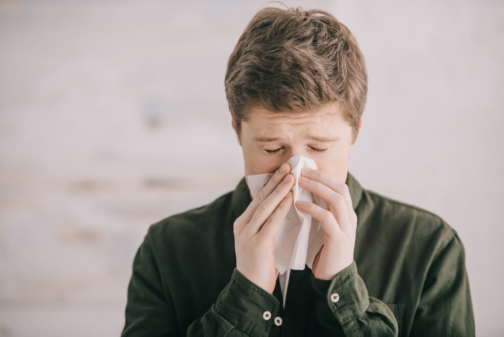 man having allergy and sneezing in tissue at home